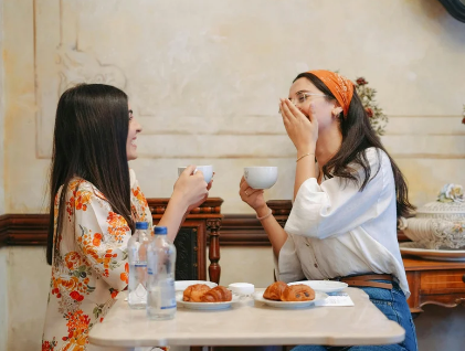 Two friends laughing over coffee and pastries at a cafe